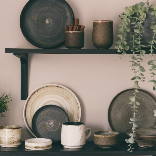 Decorative ceramic plates, mugs and plant on dark wall shelves