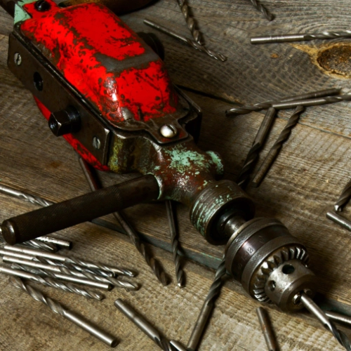 Old electric drill with metal drill bits on a wooden workbench