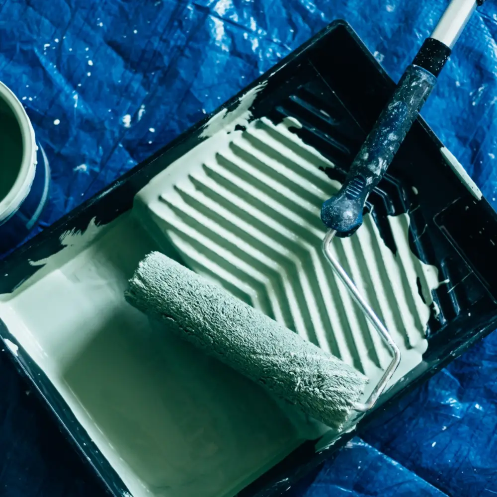 Paint roller and tray with green paint on a protective blue decorating sheet.