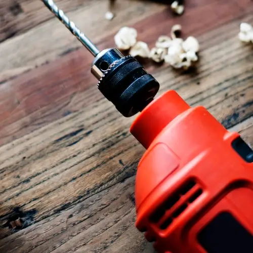 Red power drill with drill bit on a wooden workbench beside hand tools and wood shavings.